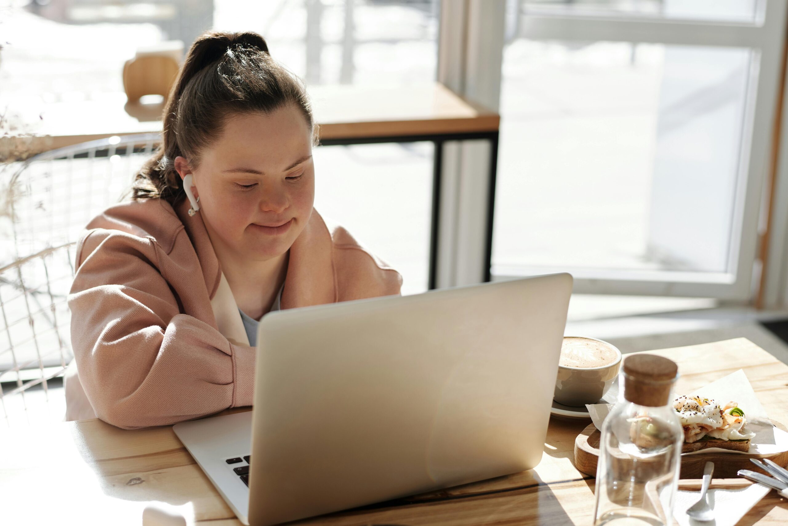 Young woman with Down syndrome using a laptop at home, enjoying coffee. Perfect for lifestyle and technology themes.